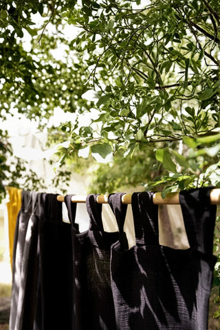 Black tab top panels outdoors under tree. Handwoven 2-layer muslin cotton curtain, Denizli, OEKO-TEX. Vivamaison.