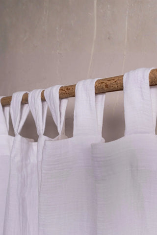 White tab loops closeup on rustic branch rod. Handwoven 2-layer muslin cotton curtain, Denizli, OEKO-TEX. Vivamaison.
