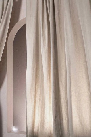 Soft folds of a beige stonewashed cotton curtain near an arched niche. Handwoven in Denizli, OEKO-TEX. Vivamaison.