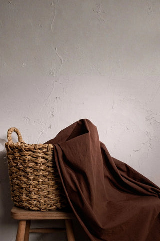 Brown stonewashed cotton curtain fabric draped over a basket. Handwoven in Denizli, OEKO-TEX. Vivamaison.