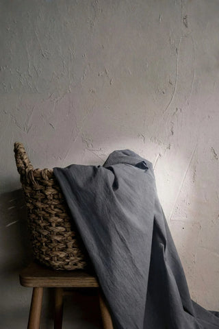 Charcoal gray stonewashed cotton curtain fabric draped over a wicker basket. Handwoven in Denizli, OEKO-TEX. Vivamaison.